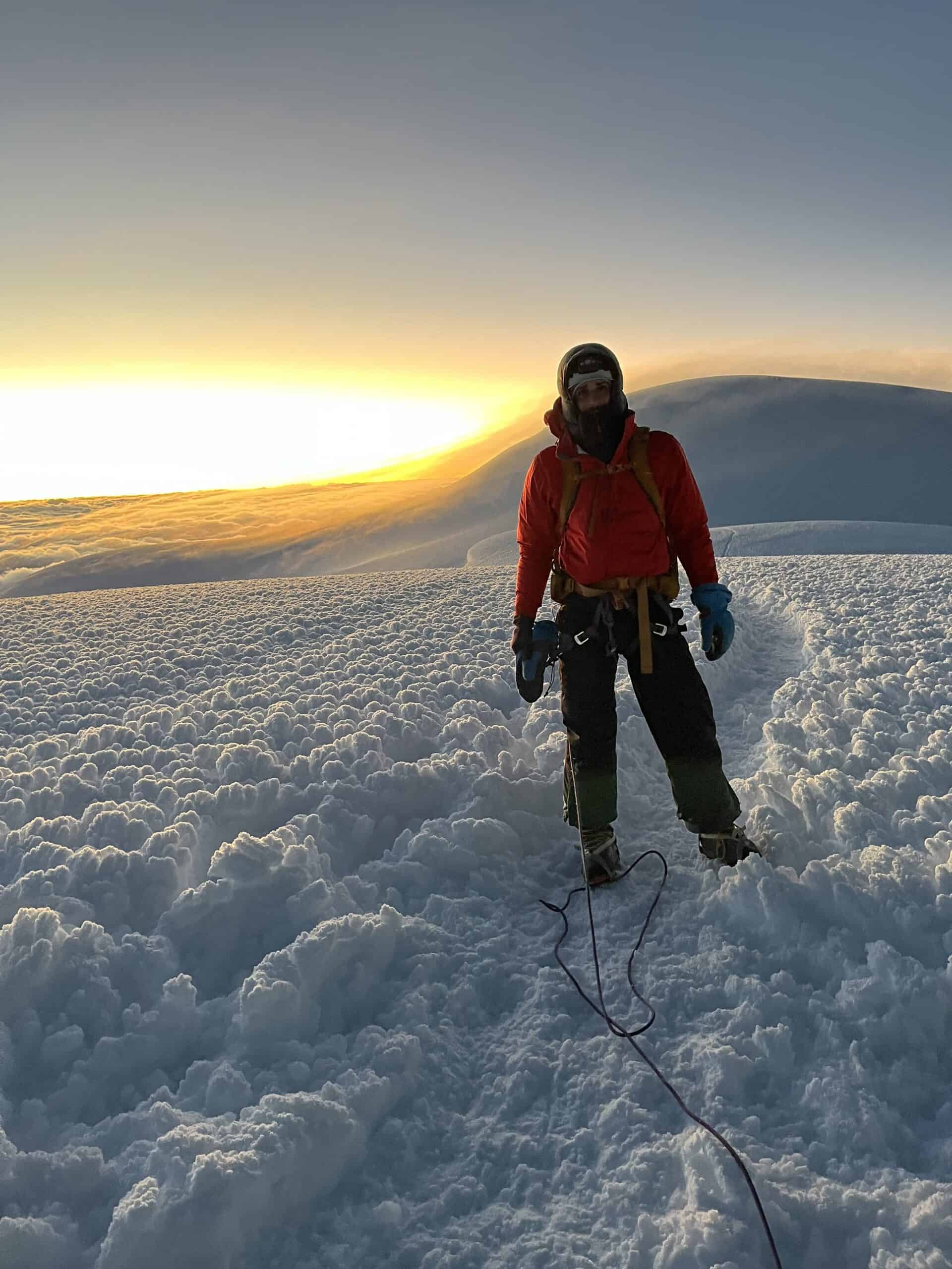 Noam standing on the summit of Chimborazo after climbing Ecuador's tallest mountain, with the sunrise in the background.