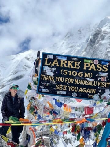 A trekker poses with the Larke Pass sign on the Manaslu Circuit trek in Nepal.