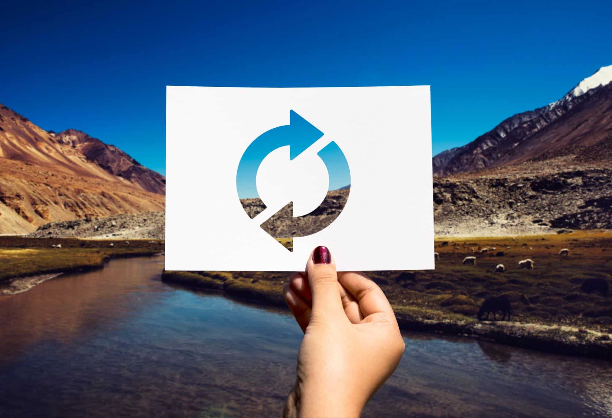 A sign held by a woman with circular arrows against a landscape (photo from Freepik).