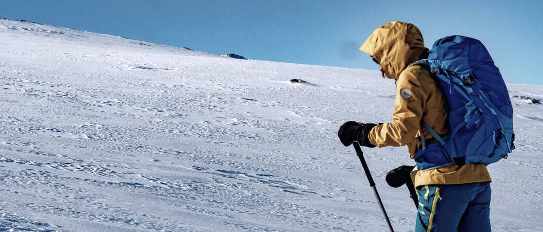 Hiker trekking across a snowy mountain slope.