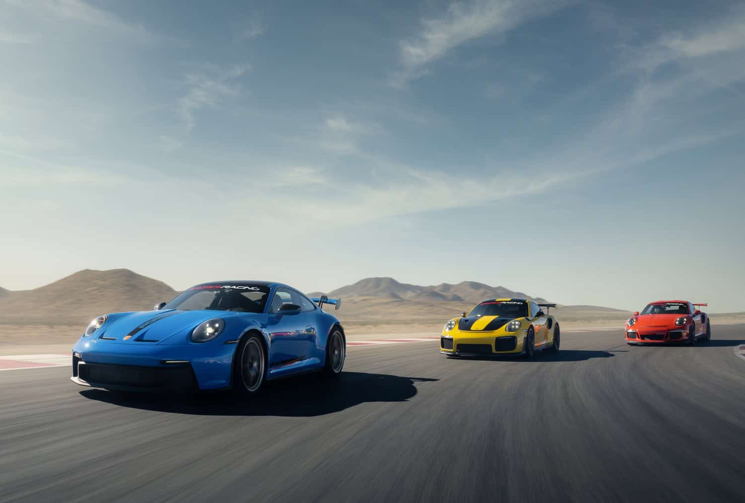 Blue, yellow, and red Porsches driving on a race track.