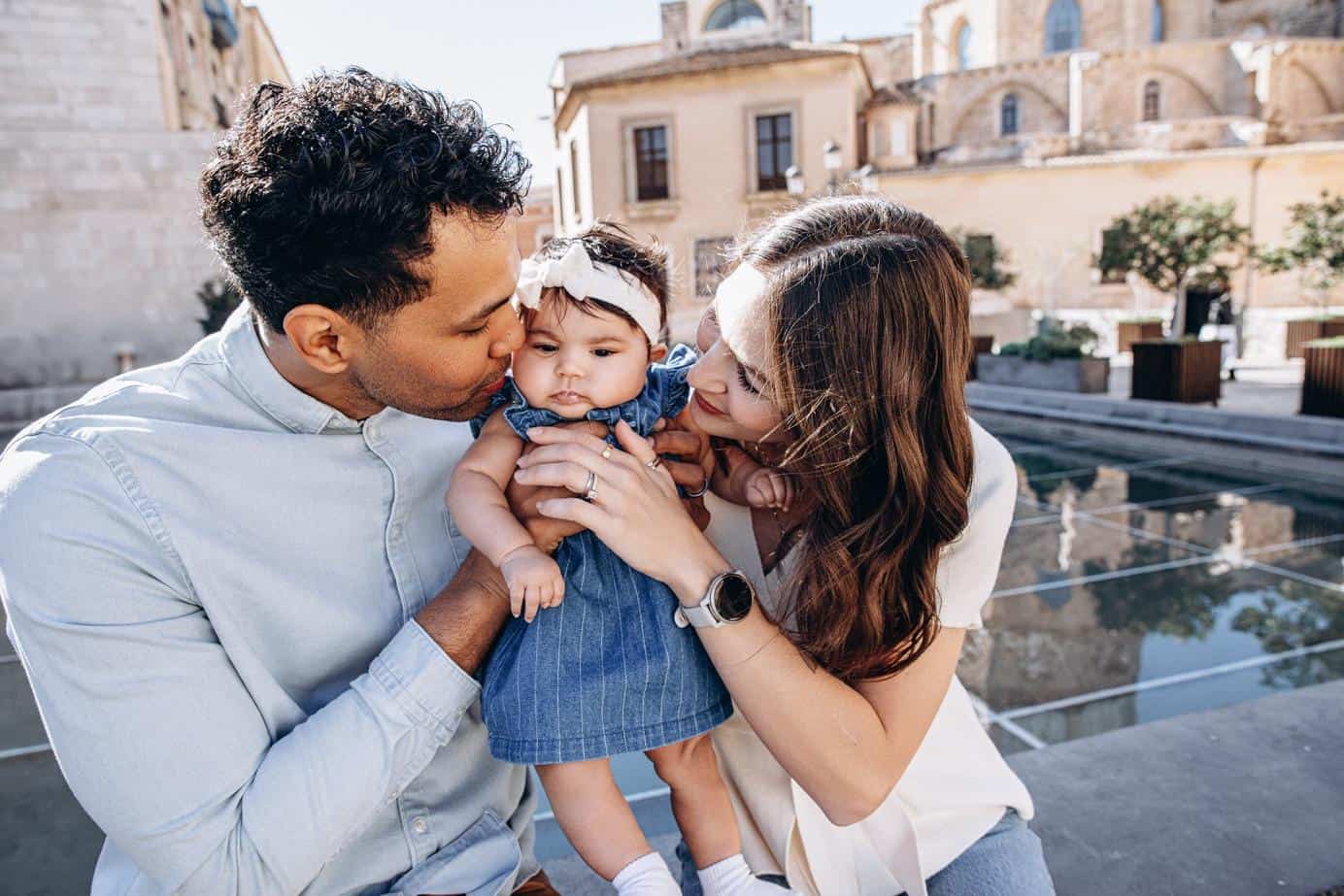 Family photoshoot at Plaza de la Virgen in Valencia with parents holding their baby girl in gentle golden light.