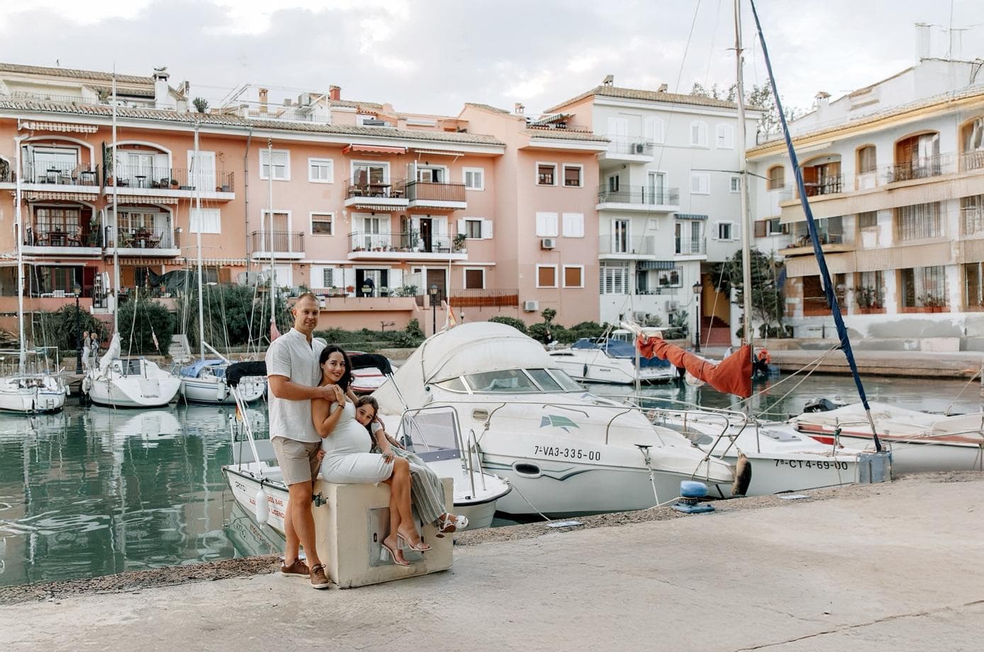 Maternity photoshoot in Valencia at Marina Port Saplaya with family posing by boats and colorful waterfront houses.