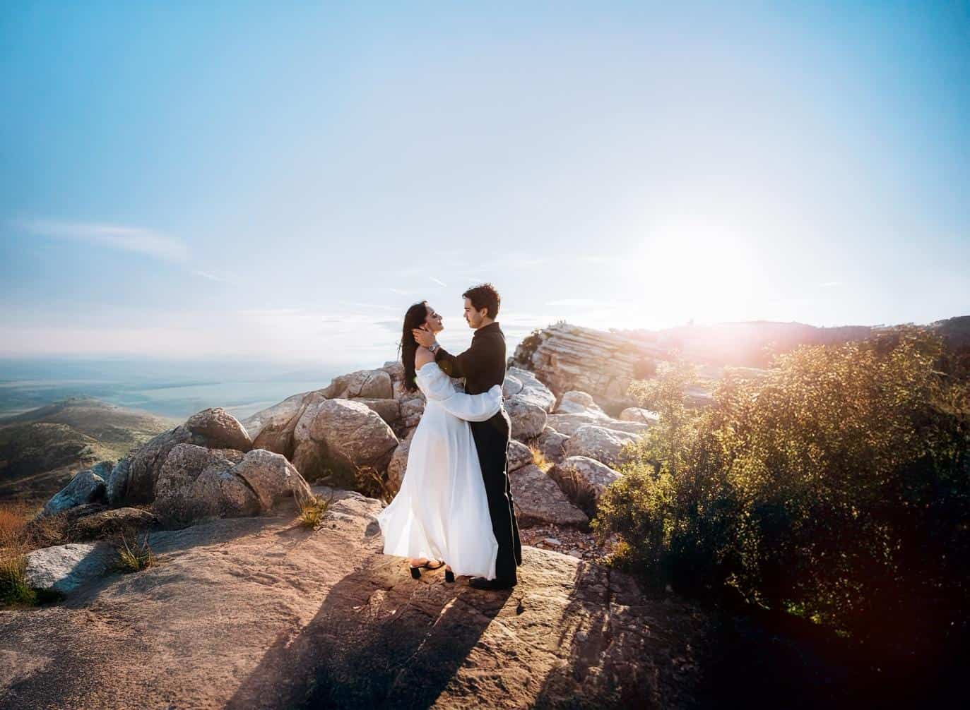 Romantic proposal photoshoot in Valencia with a couple embracing on a stony hill at sunset with panoramic landscape view.