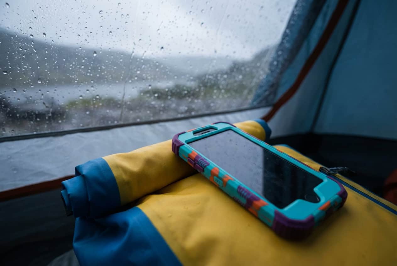 Smartphone cases are travel tech essentials, shown inside a rainy tent window.