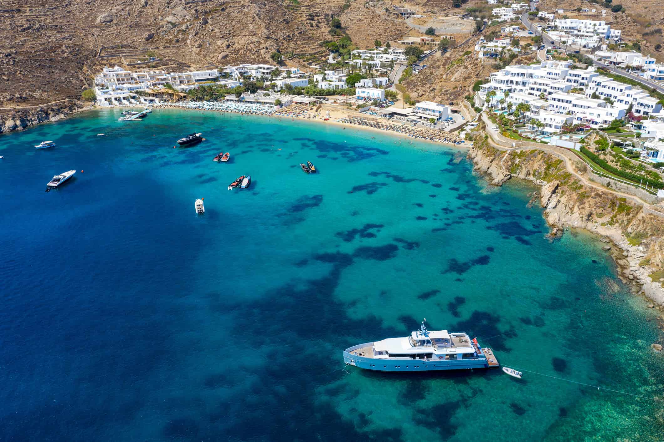 Yacht anchored in turquoise water near a coastline, illustrating yacht vs hotel travel experience