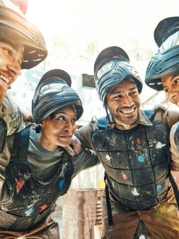 Travelers in protective gear smiling after a paintball game at an outdoor adventure park