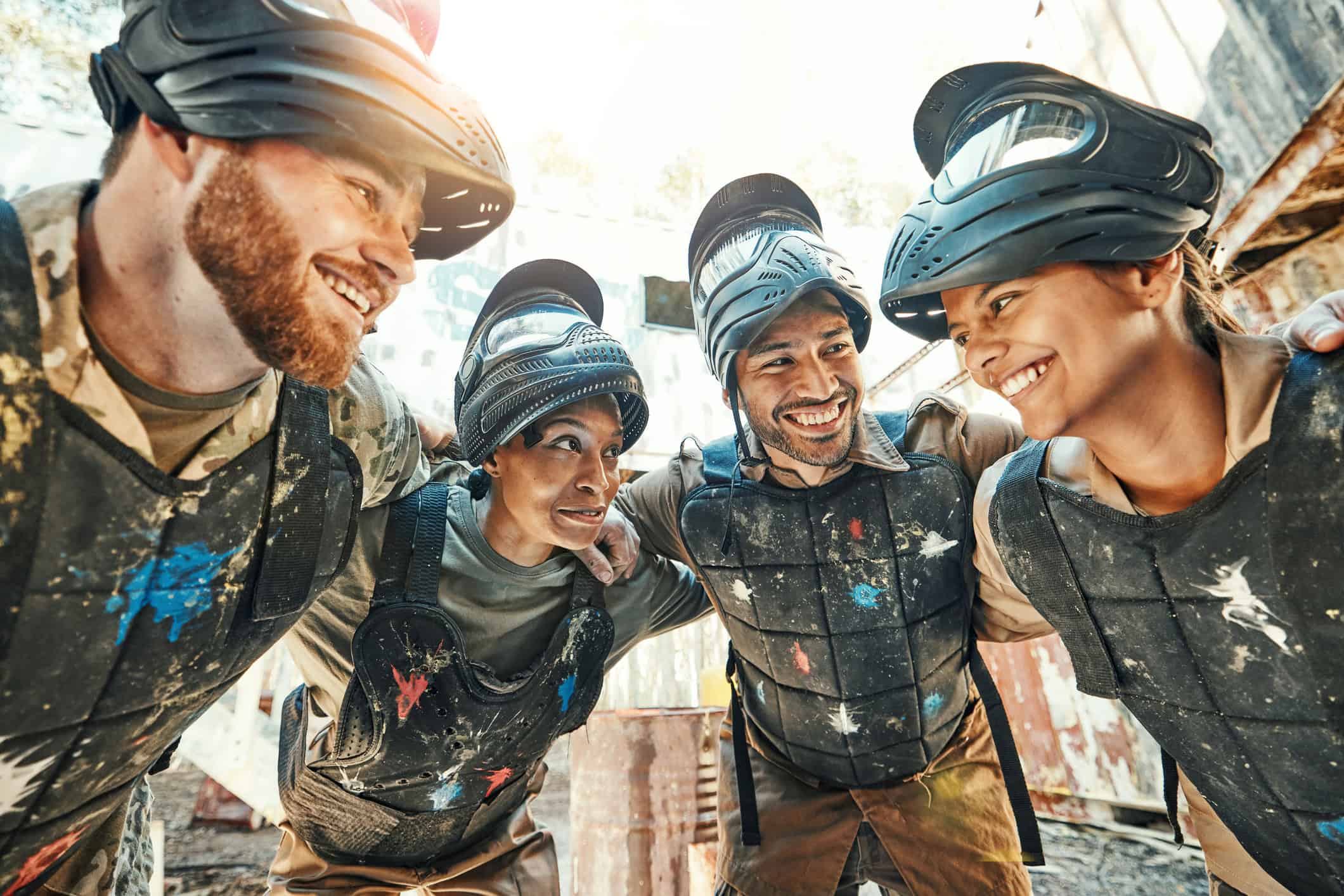 Travelers in protective gear smiling after a paintball game at an outdoor adventure park