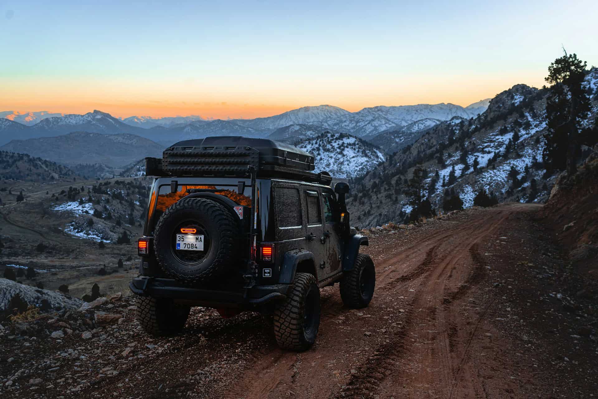 Off-road vehicle driving on a remote mountain road at dusk during a road trip