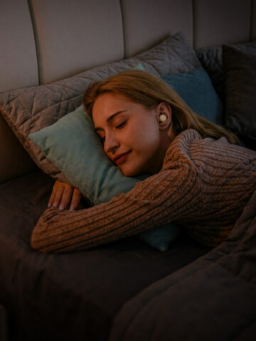 Woman sleeping on her side while wearing Fitnexa SomniPods 3 sleep earbuds.