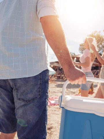 Friends carrying a cooler onto the beach for a summer picnic