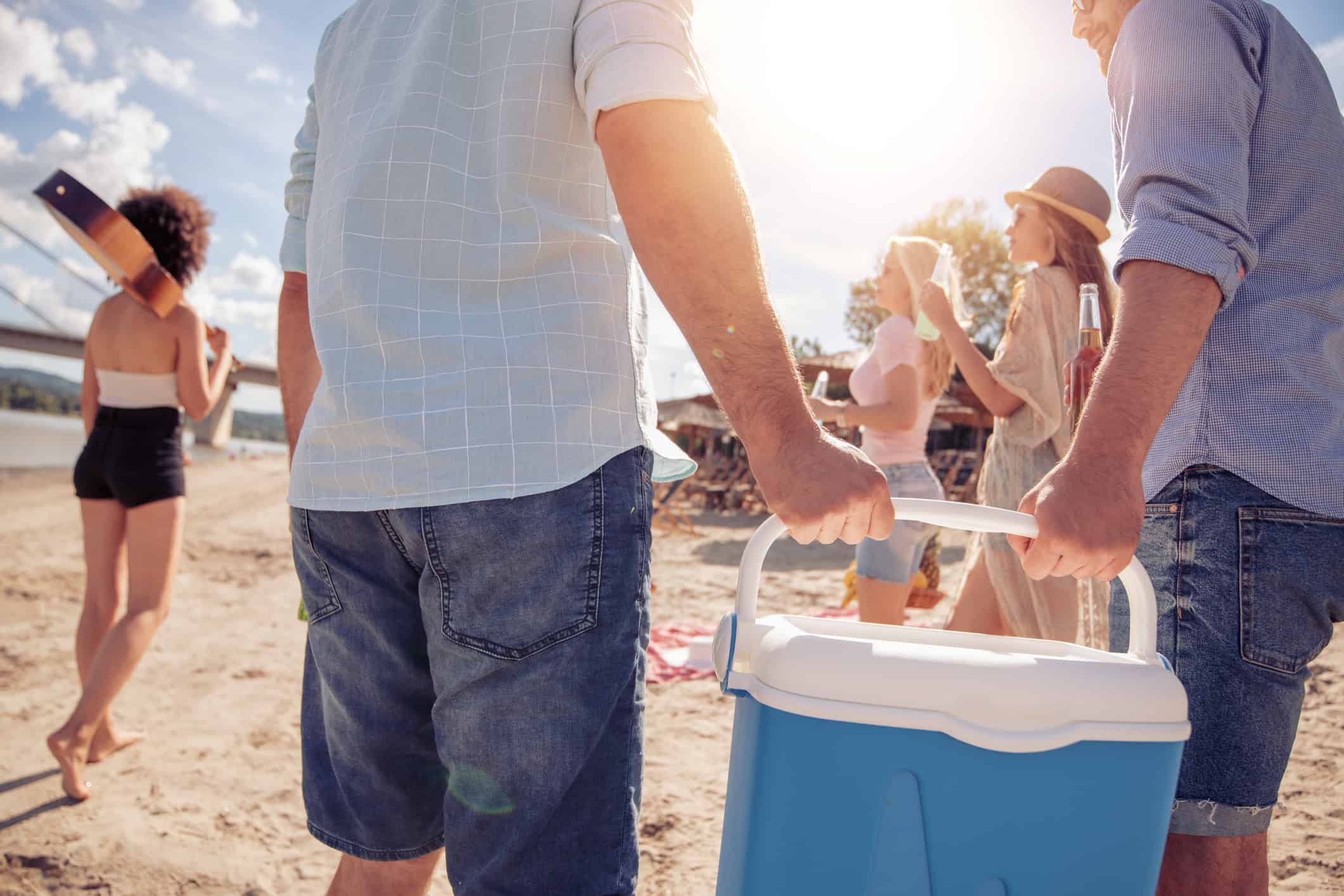 Friends carrying a cooler onto the beach for a summer picnic
