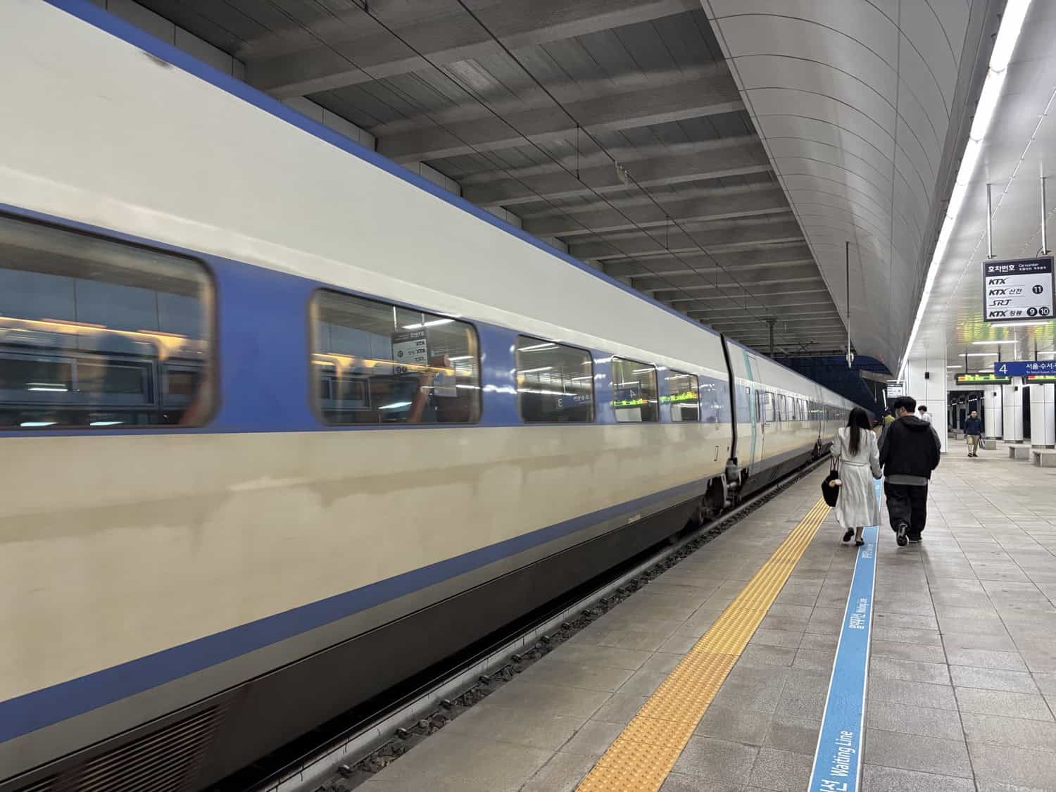 A KTX-I bullet train at a Seoul platform as two travelers walk alongside it