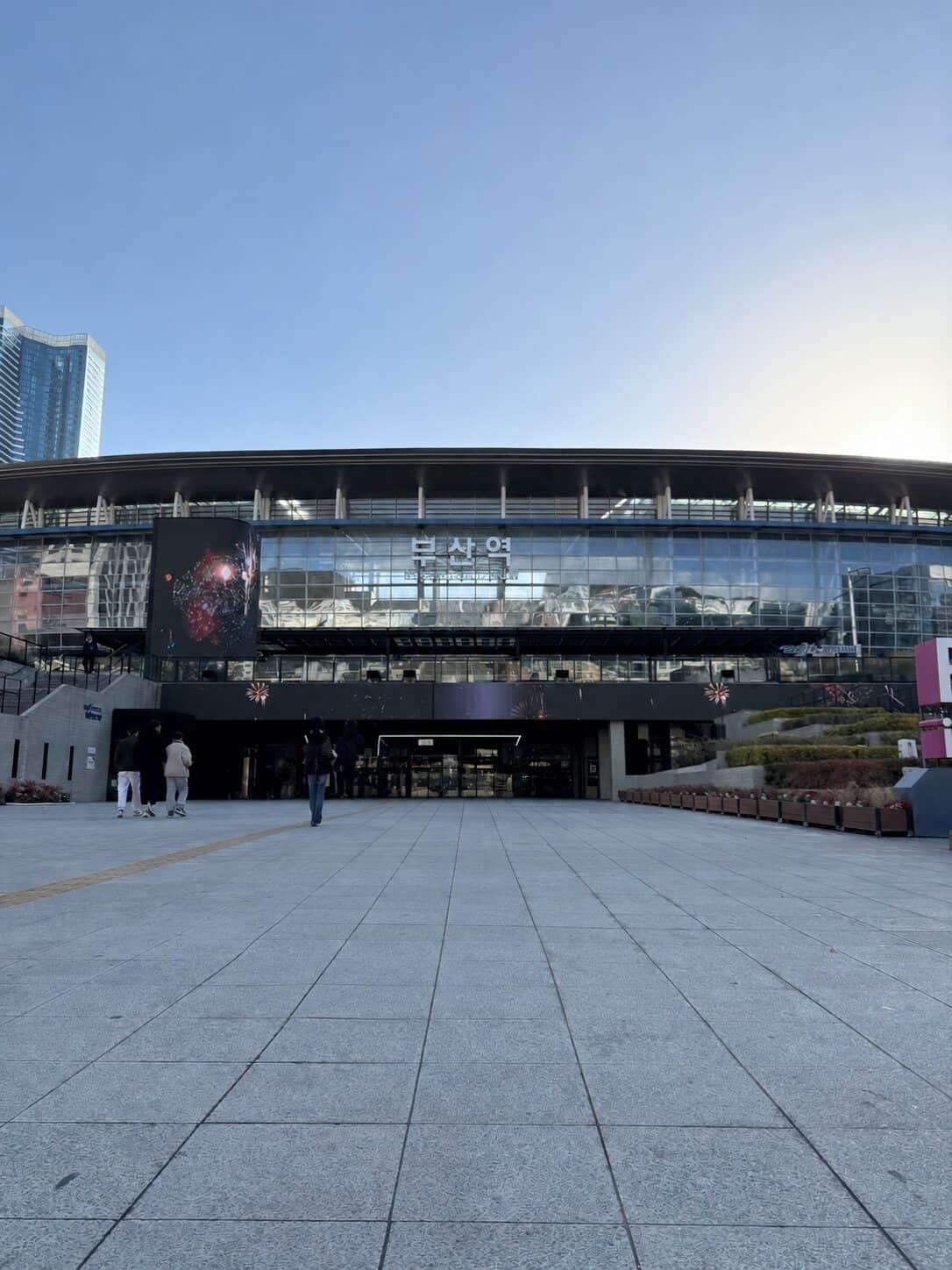 Busan Station lit up at blue hour, its curved roofline under an evening sky