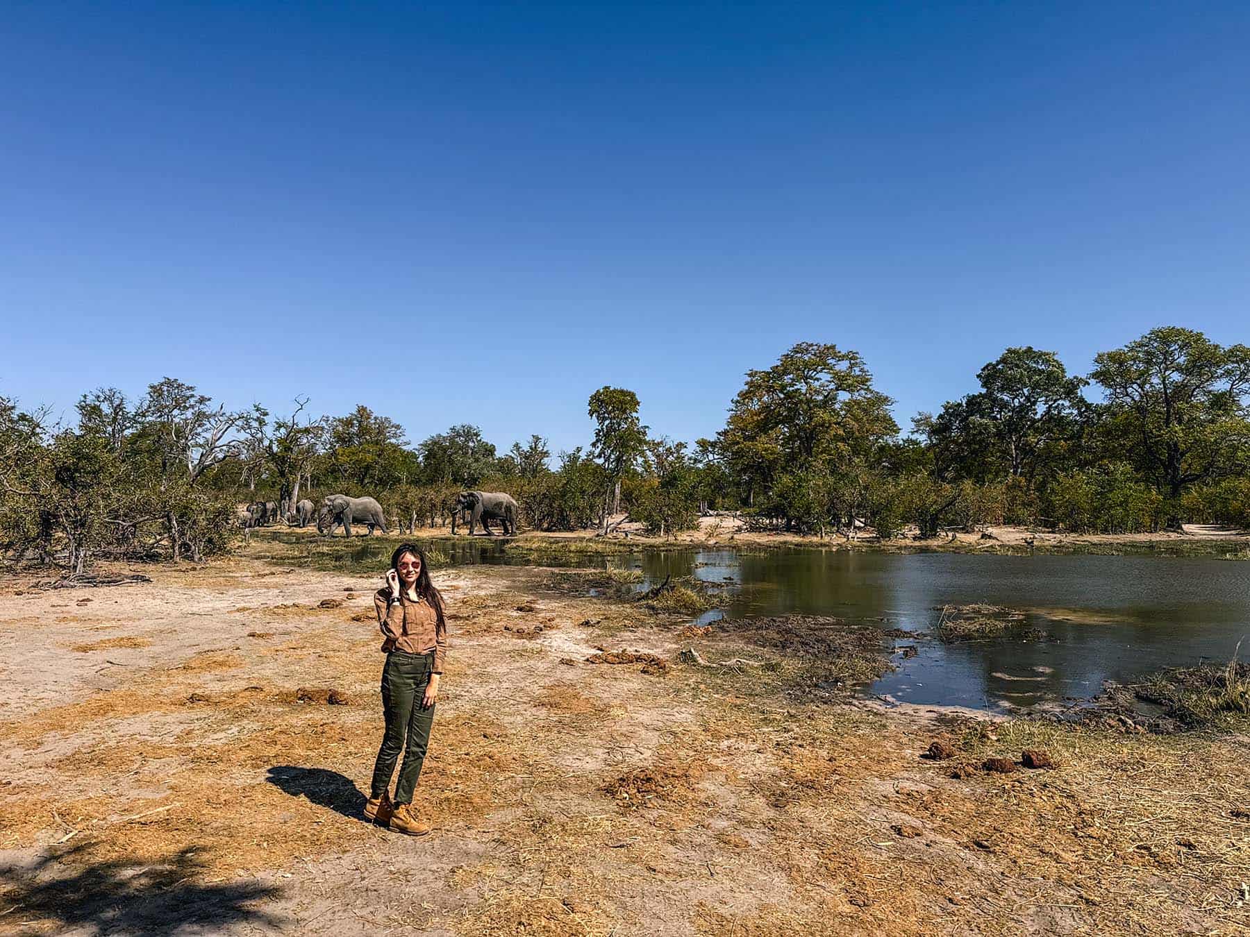 Ella standing in front of a river in the Okavando Delta with elephants in the background