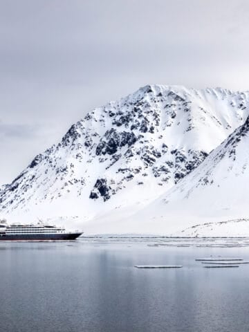 Cruise ship sailing beneath snow-covered mountains in a Svalbard fjord