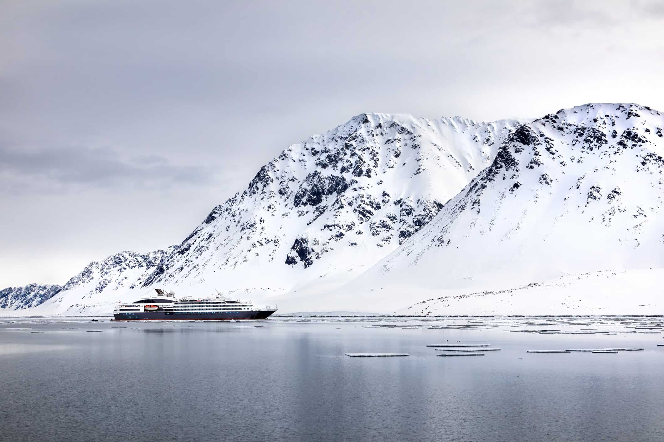 Cruise ship sailing beneath snow-covered mountains in a Svalbard fjord