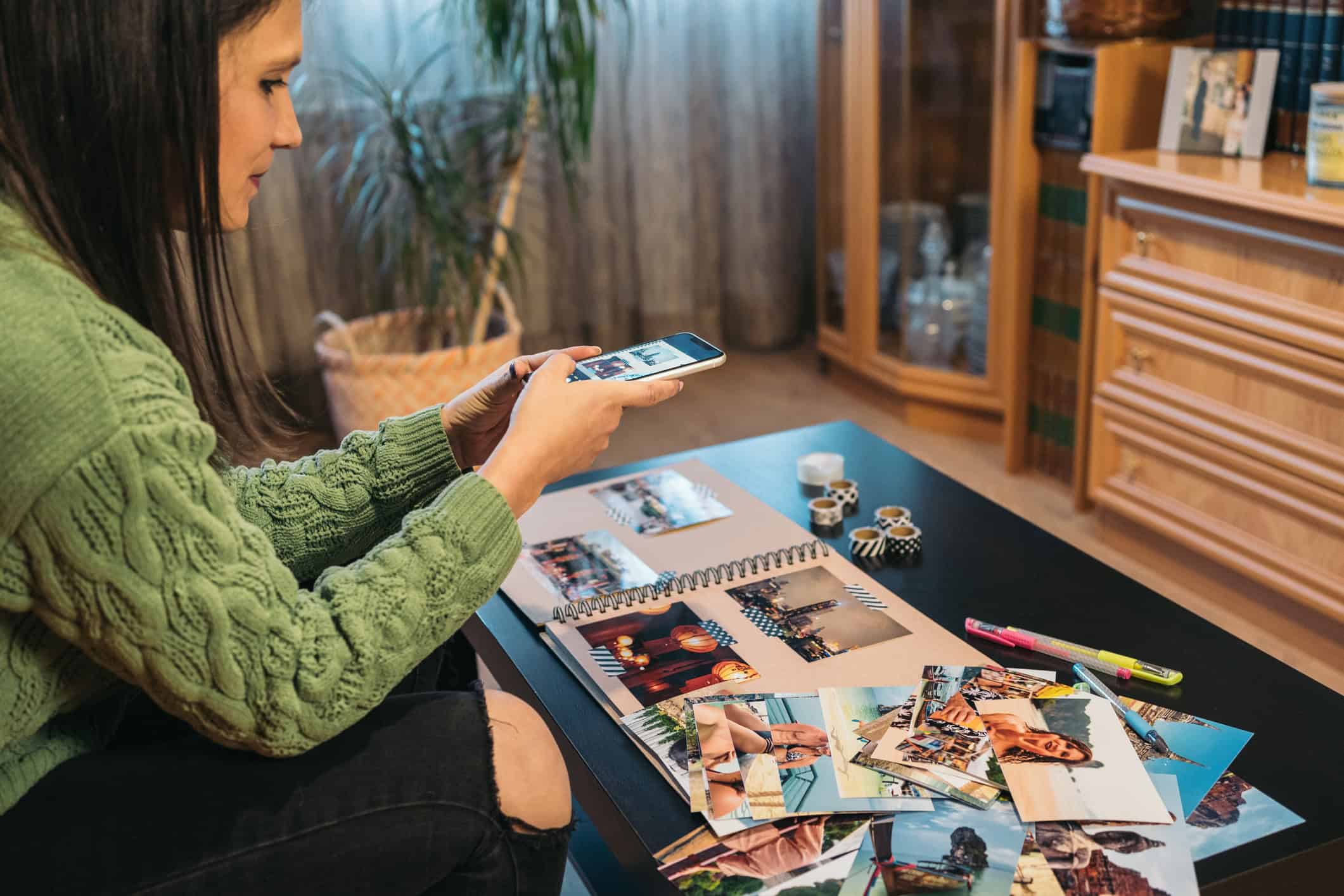 A woman arranging printed travel photos in a scrapbook at home.