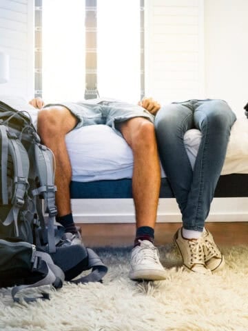 Two tired backpackers lying across a bed after returning from a trip.