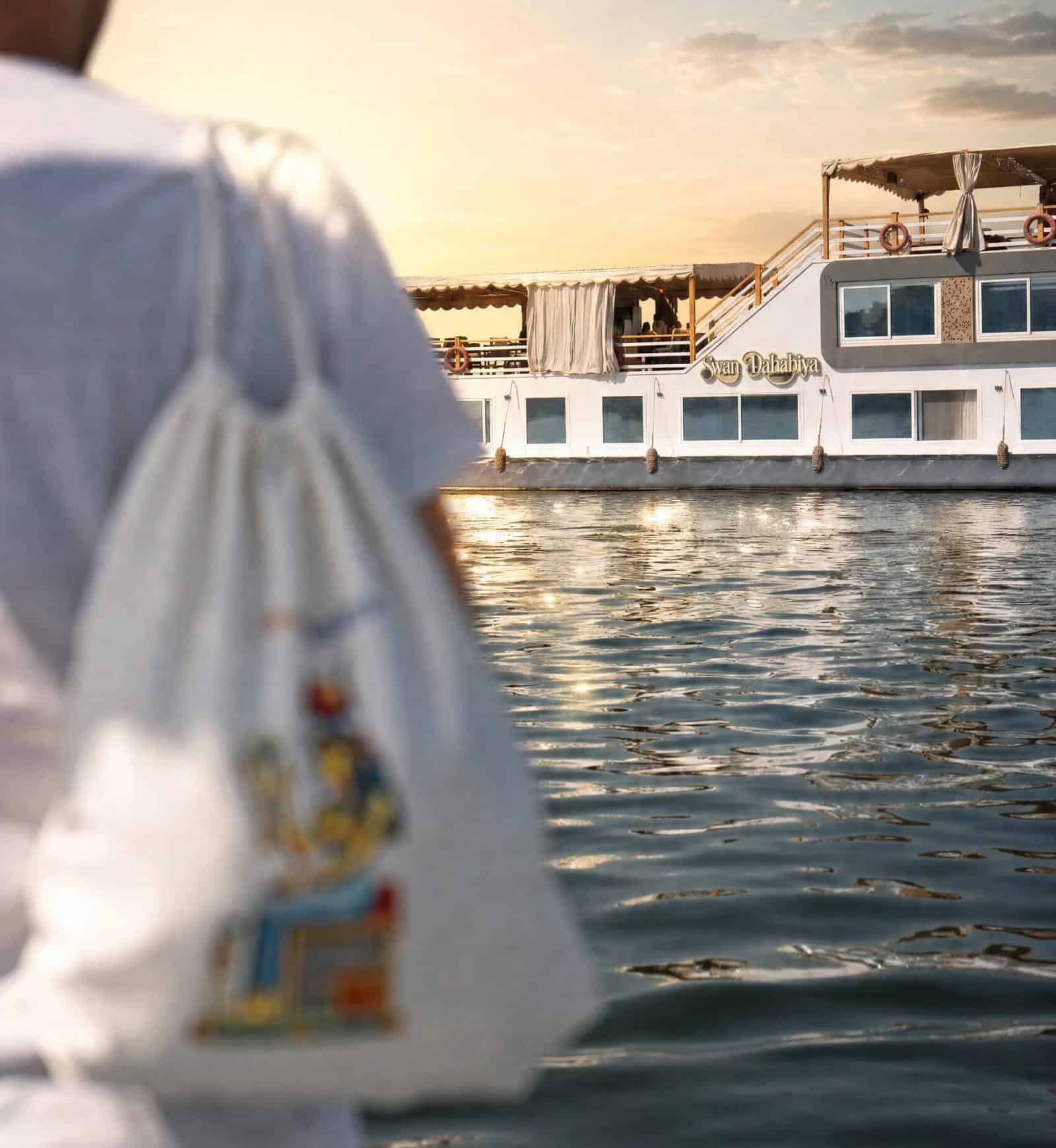 Swan Dahabiya on the Nile at sunset, viewed past a person in white