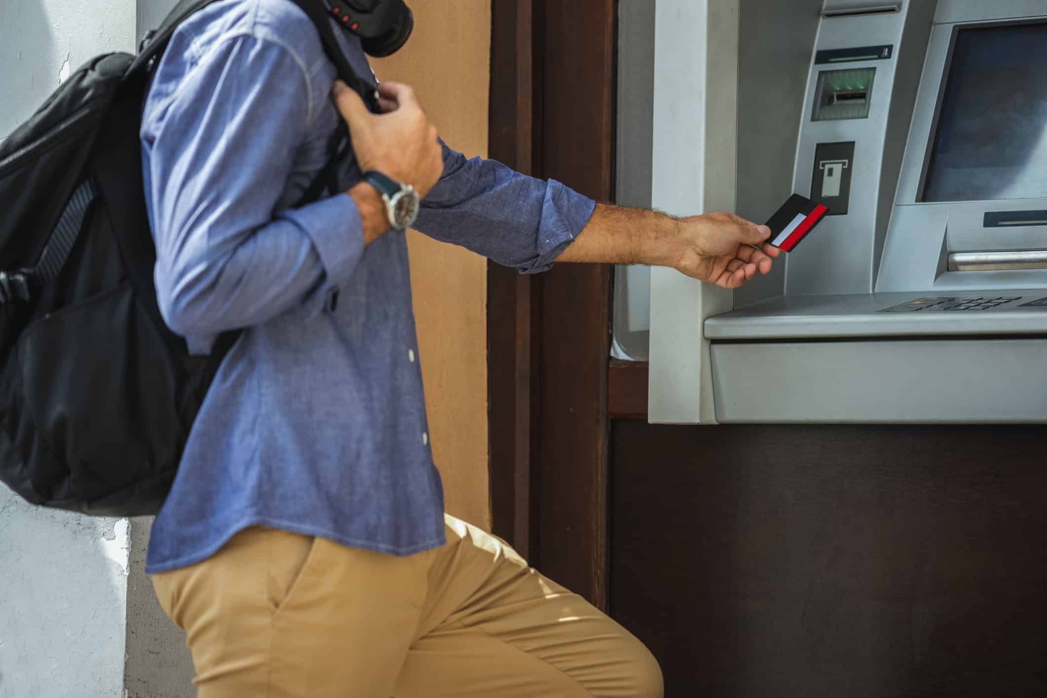 Traveler with a backpack using a bank card at an ATM abroad