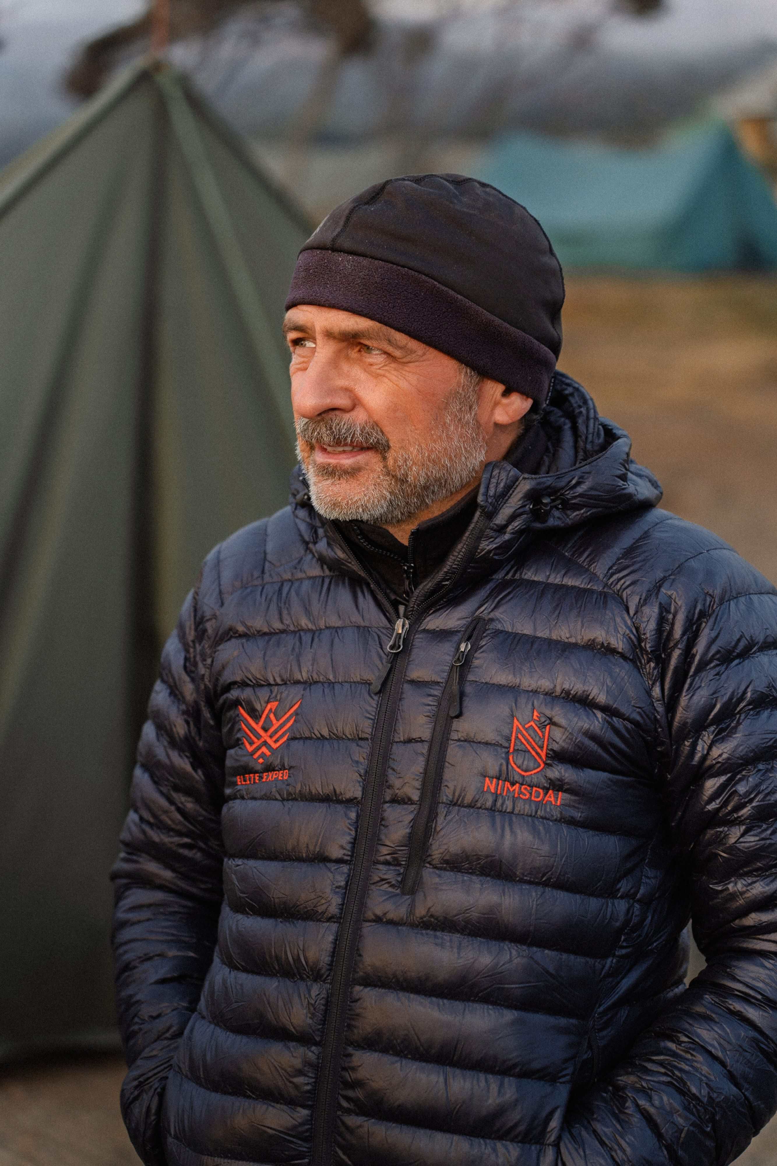 Yevgen Staroselskiy wearing a black beanie and down jacket in front of expedition tents.